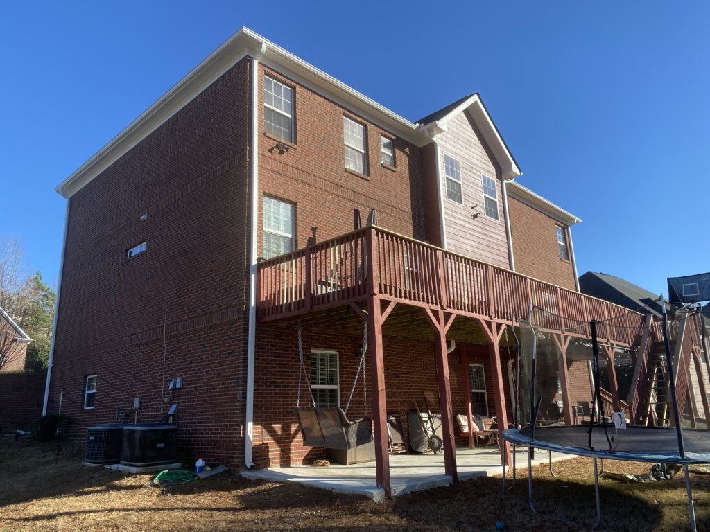 A large brick house with a large deck and a trampoline in the backyard.