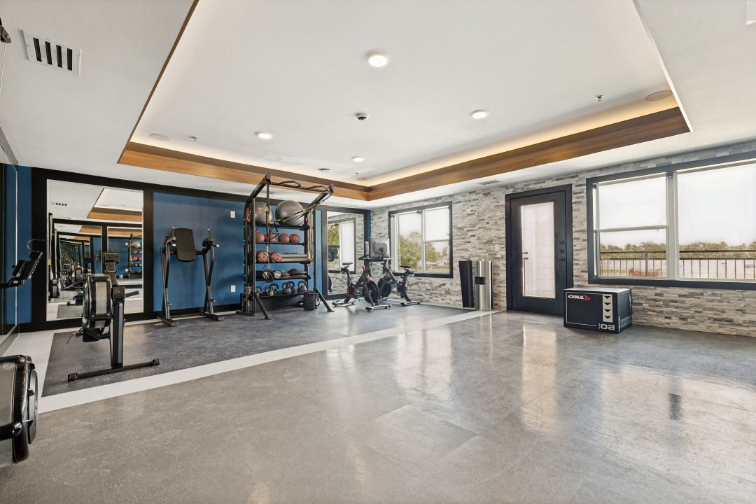 Modern gym with weight machines, mirrored walls, large windows, and polished concrete floor