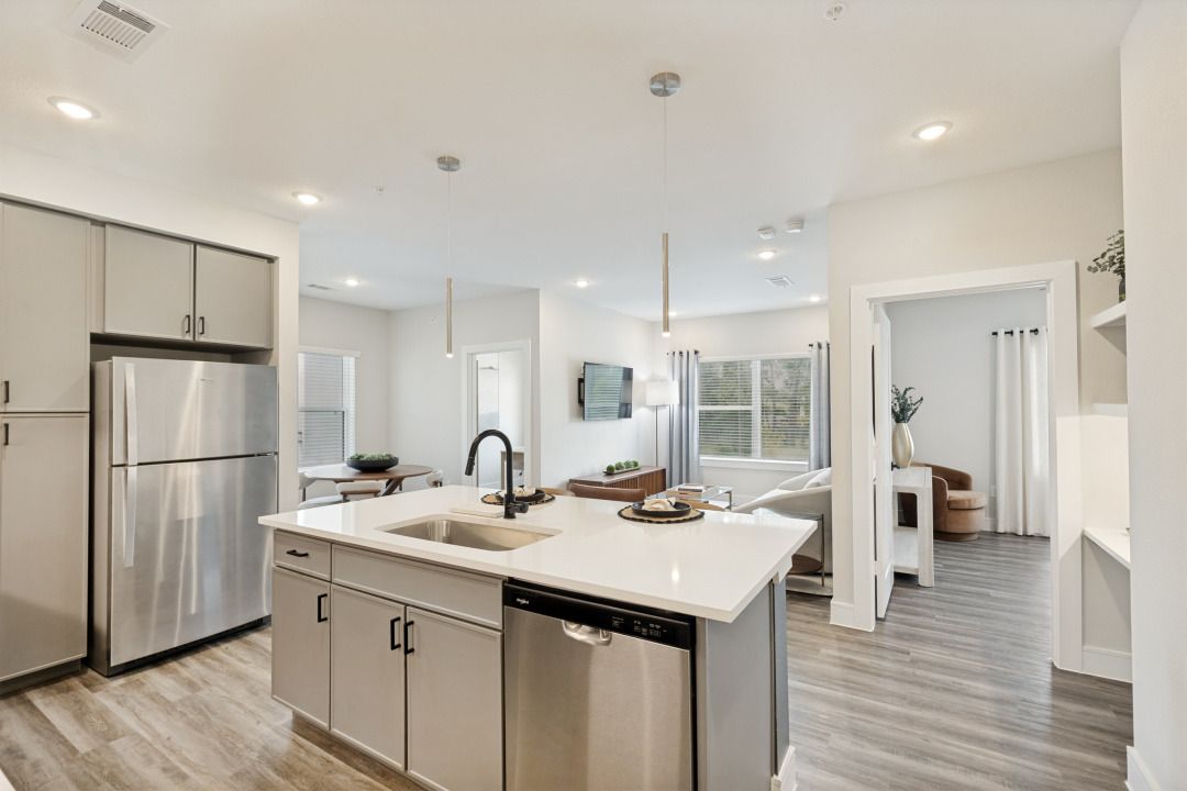 Bright modern kitchen with stainless appliances, white island, and open view into adjacent room