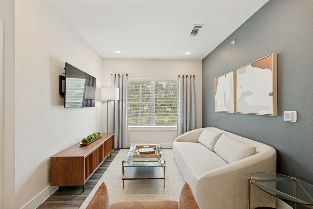 Modern living room with white sofa, wall-mounted TV, coffee table, and large window.