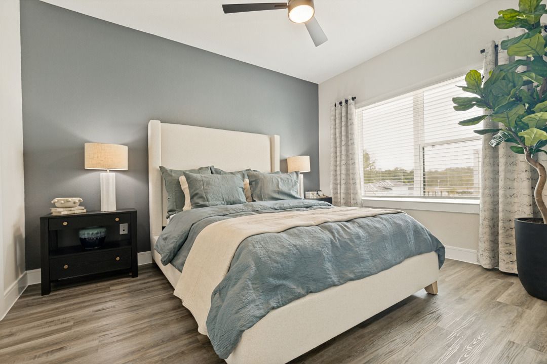 Modern bedroom with a blue bedspread, nightstand lamp, and large window with blinds
