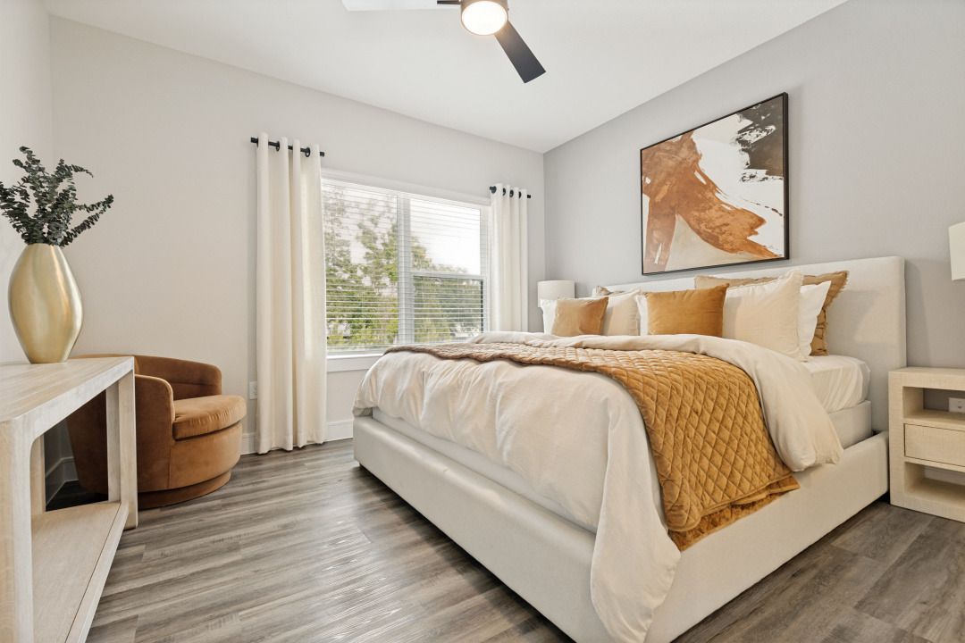 Bright modern bedroom with a white bed, tan throw, abstract wall art, and window seating area