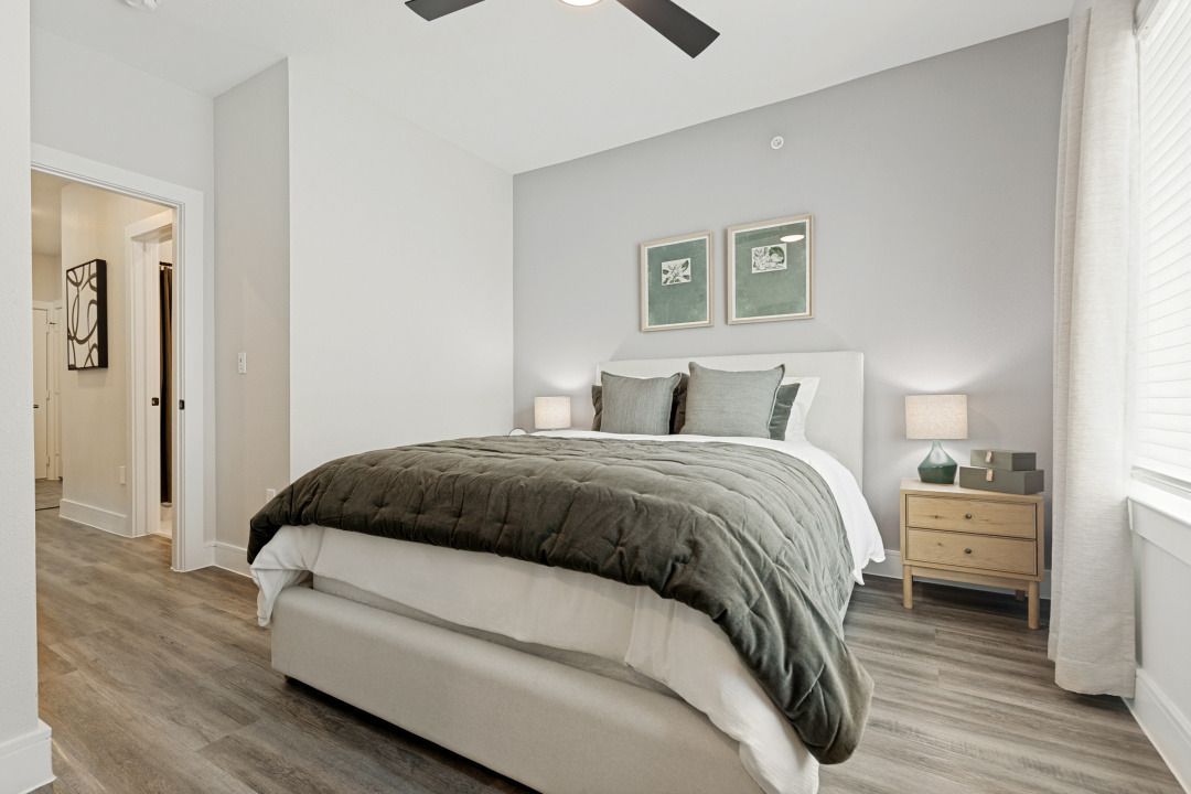 Bright bedroom with a bed, gray bedding, nightstands, and framed wall art