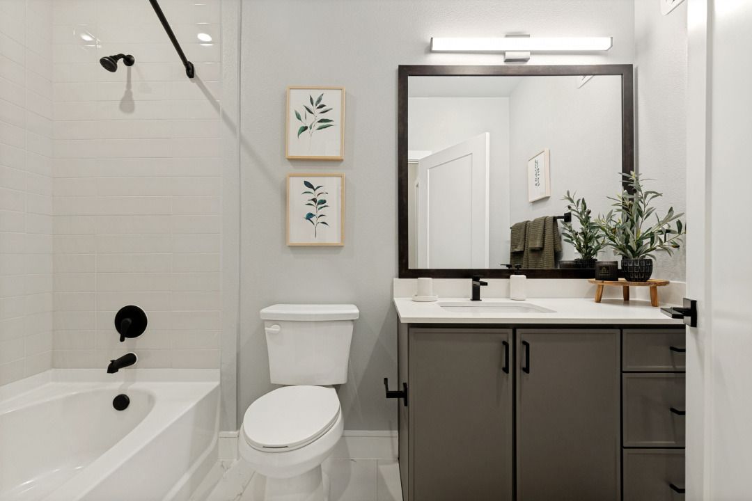 Modern white bathroom with bathtub, toilet, vanity, mirror, and small wall art.