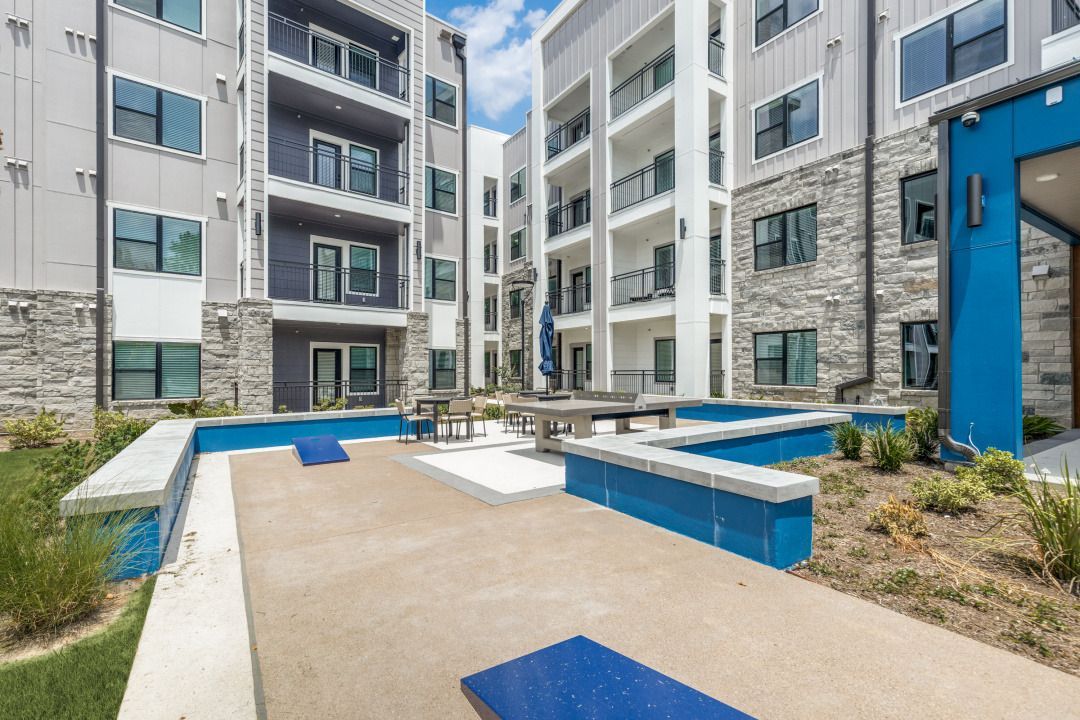 Modern apartment courtyard with blue benches, concrete paths, and landscaped planters between buildings