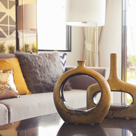 Two gold decorative vases on a dark table in a living room with pillows.