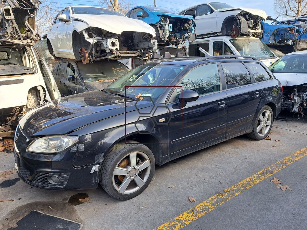 Un'auto nera è parcheggiata davanti a un mucchio di auto distrutte.