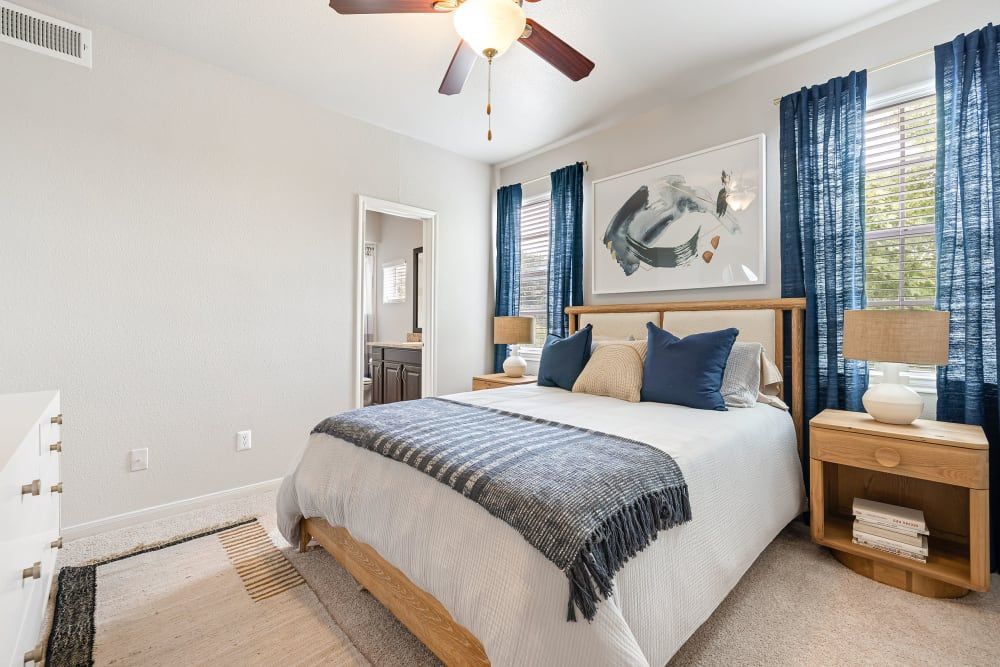 Apartment bedroom with a large bed and a ceiling fan at Marquis at Stonegate offers apartments for rent near White Settlement, TX.