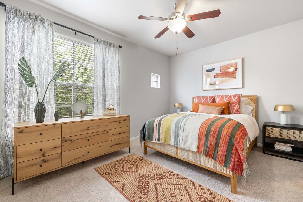 Apartment bedroom with a bed, dresser, nightstand, and ceiling fan at Marquis at Stonegate offers apartments for rent near Saginaw, TX.