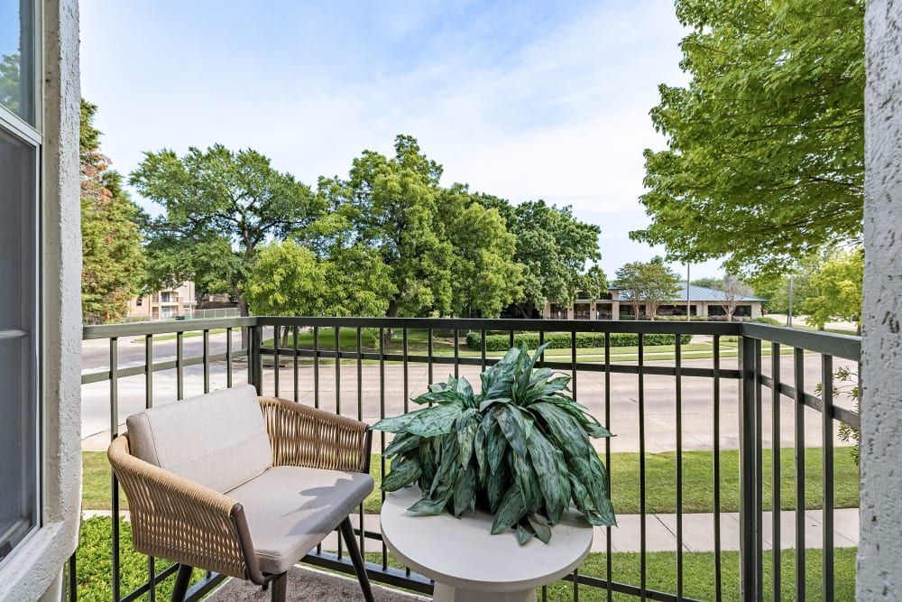 Apartment balcony with a chair, table, and potted plant at Marquis at Stonegate offers pet-friendly apartments in Fort Worth, TX.