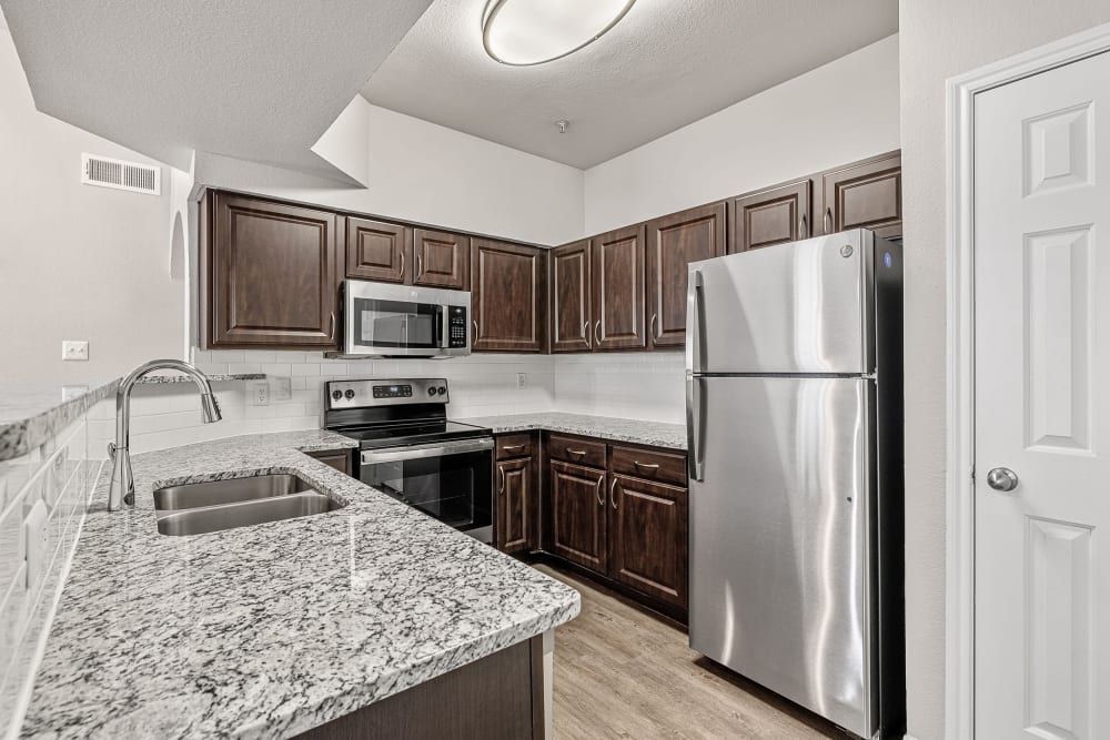 Apartment kitchen with granite countertops, stainless steel appliances, and a refrigerator at Marquis at Stonegate offers apartments near TCU in Fort Worth, TX.