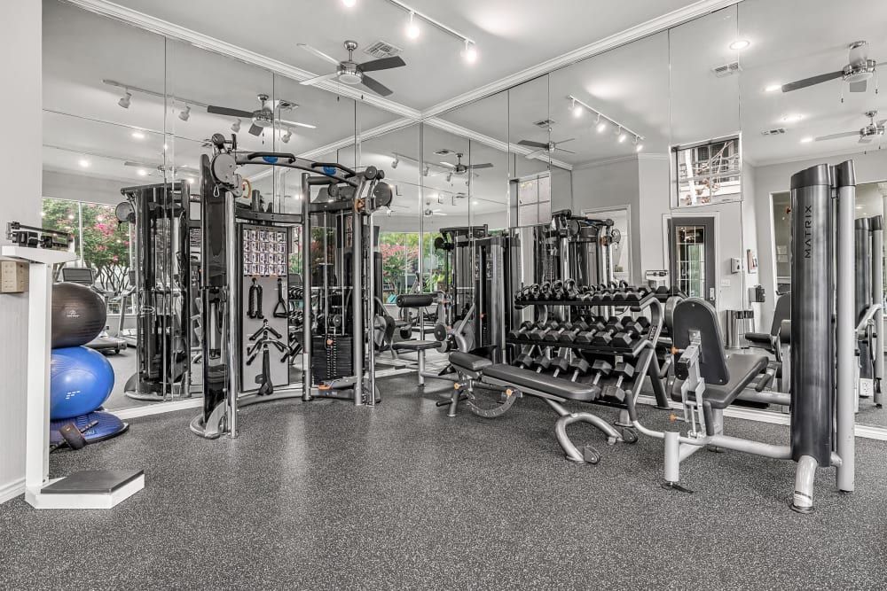 A large gym filled with lots of exercise equipment and mirrors at Marquis at Stonegate offers apartments near Texas Christian University in Fort Worth, TX.