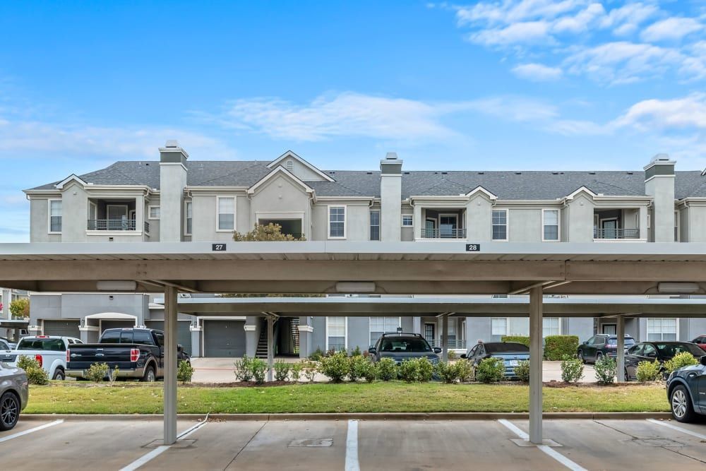 Apartment parking lot with cars parked under a canopy at Marquis at Stonegate offers apartments for rent in Fort Worth, TX.