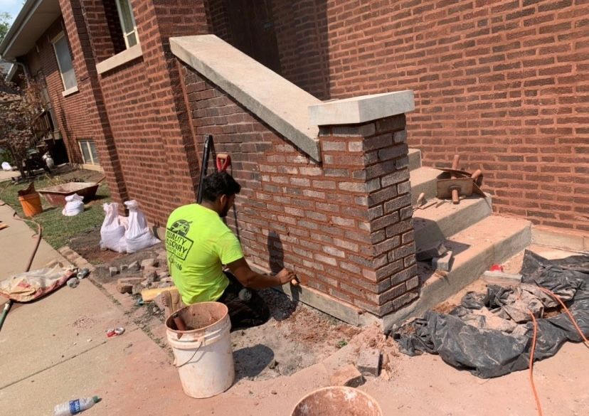 A man is working on a brick wall outside of a house.