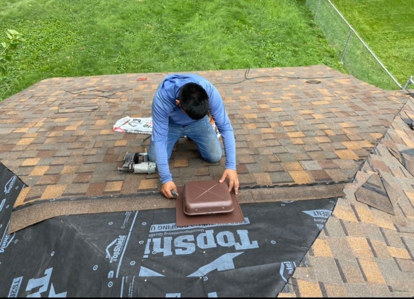 A man is kneeling on top of a roof while working on it.