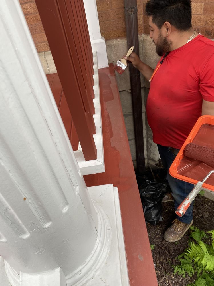 A man in a red shirt is painting a porch with a brush.