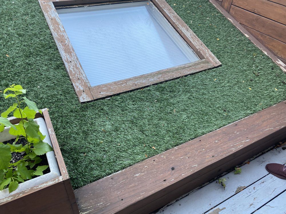 A wooden deck with a planter and a skylight on top of it.