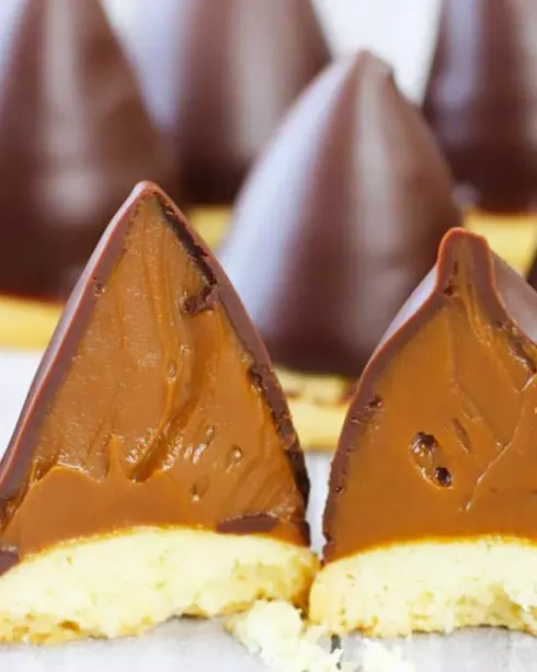 Galletas de merengue bañadas en chocolate con relleno de caramelo sobre una superficie blanca.