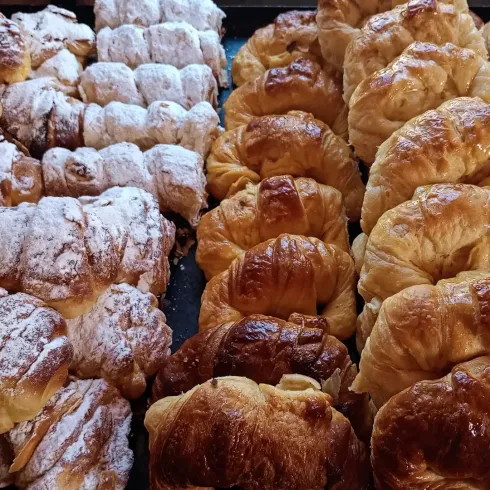 Surtido de croissants y pasteles espolvoreados con azúcar glas en una bandeja de panadería.