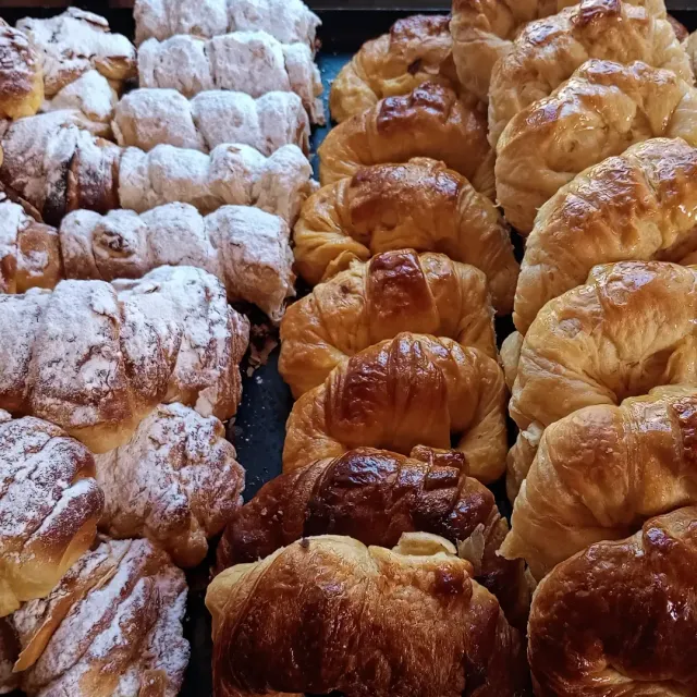 Surtido de croissants y pasteles espolvoreados con azúcar glas en una bandeja de panadería.