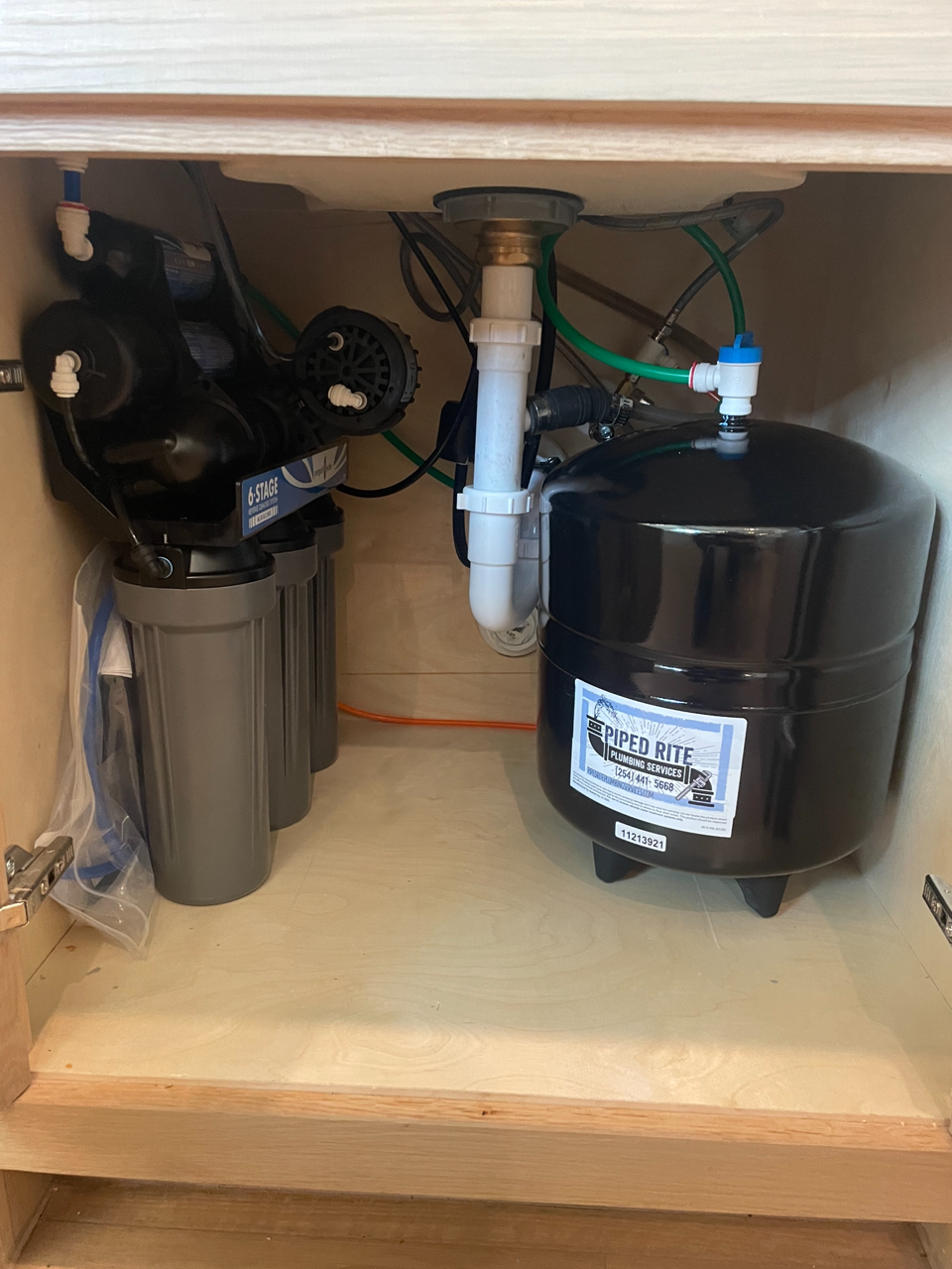 A water filter is under a sink in a cabinet.