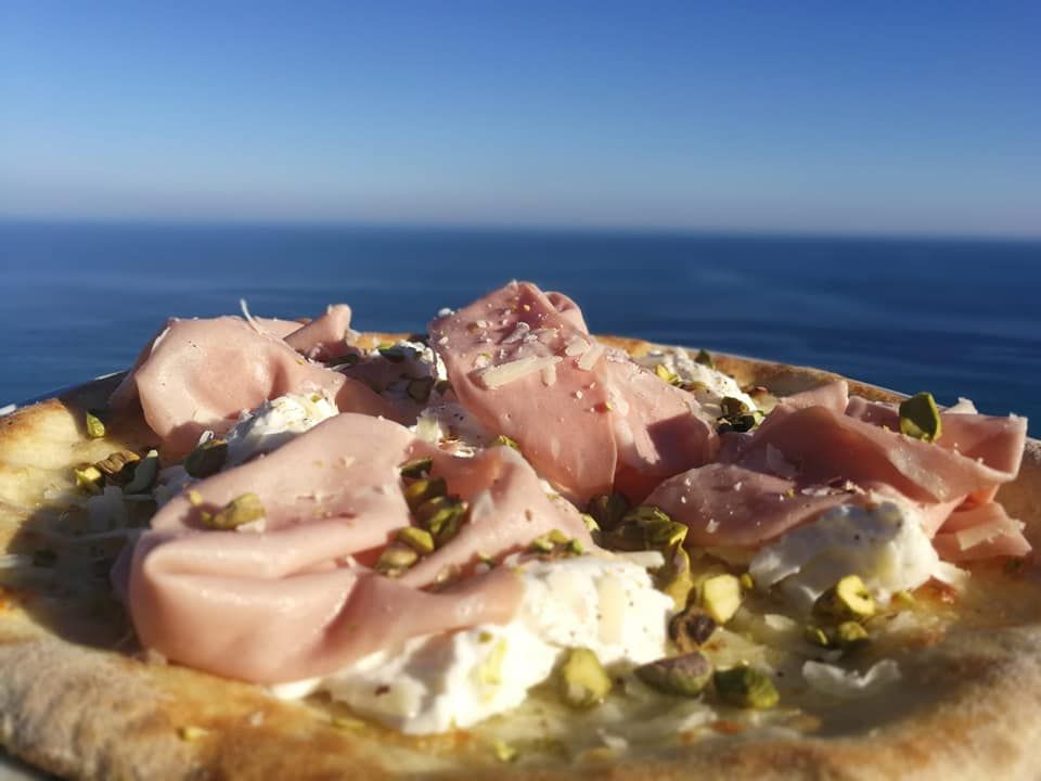 Una pizza con prosciutto e pistacchi è seduta di fronte all'oceano