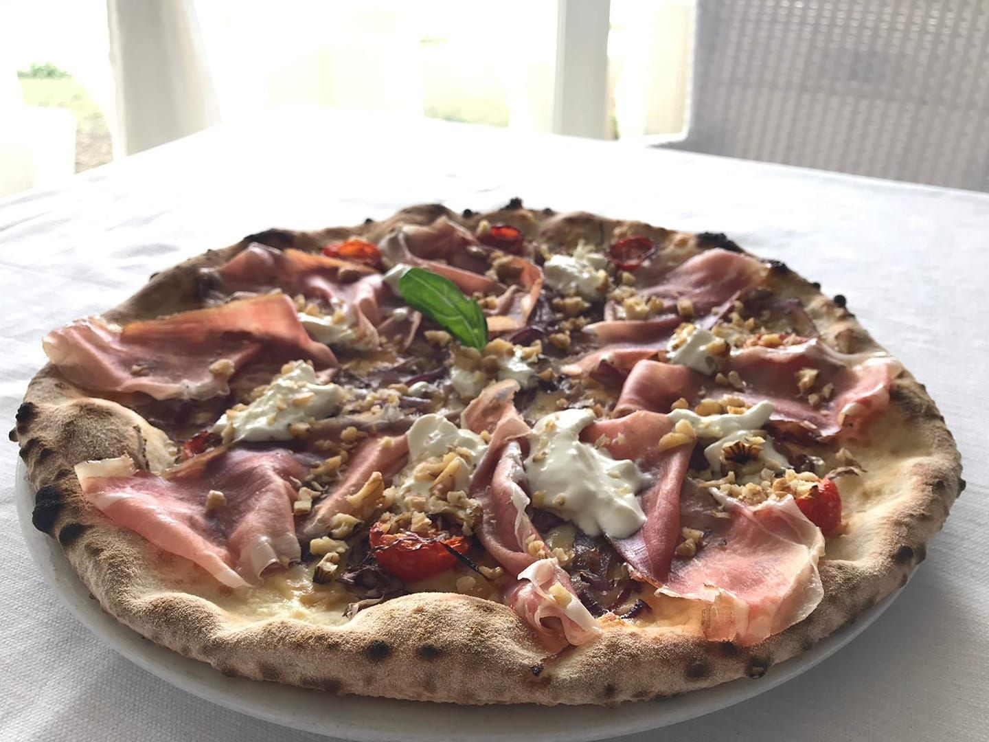 Una pizza con prosciutto e pomodori su un piatto bianco