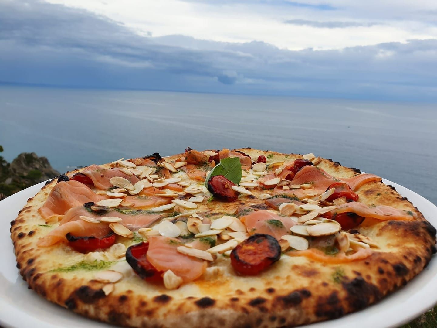 Una pizza su un piatto bianco con l'oceano sullo sfondo