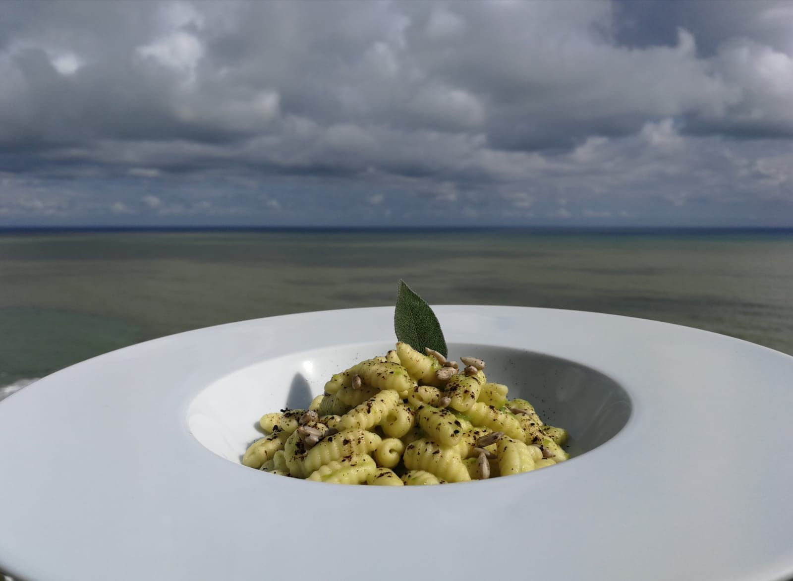 Un piatto di pasta con una foglia verde sopra di fronte al mare
