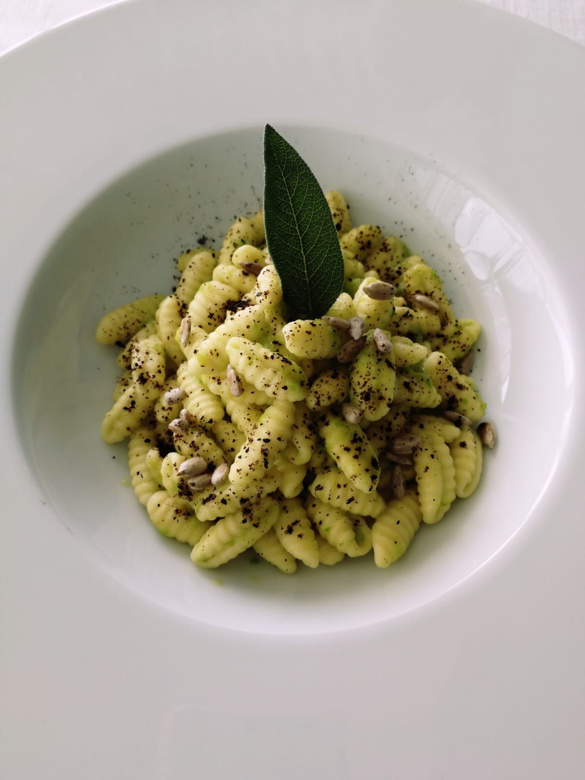Un piatto bianco con sopra la pasta e una foglia di salvia.