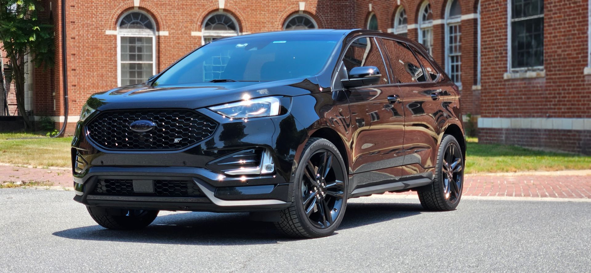 Black SUV parked on a road in front of a brick building. The car is shiny and the wheels are black.
