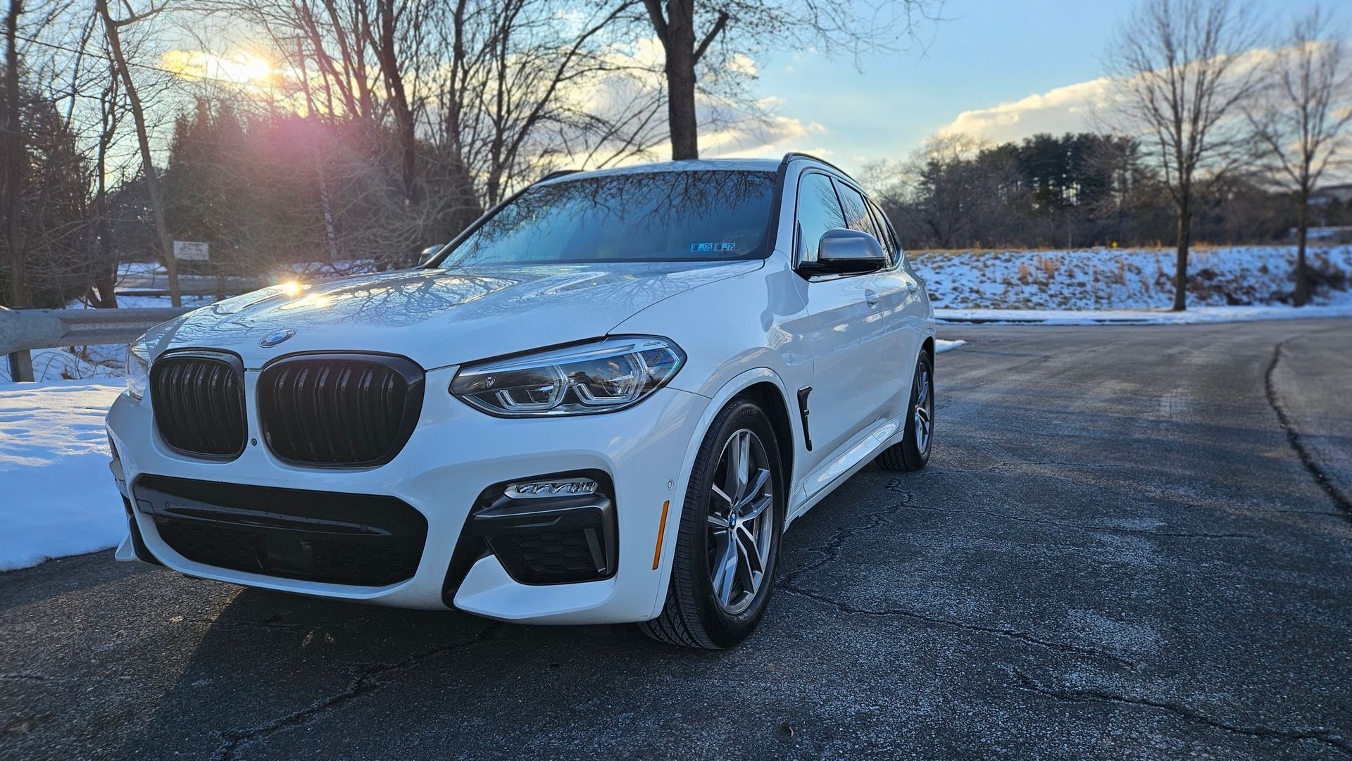 White BMW X3 SUV parked on a snowy driveway with the sun setting in the background.