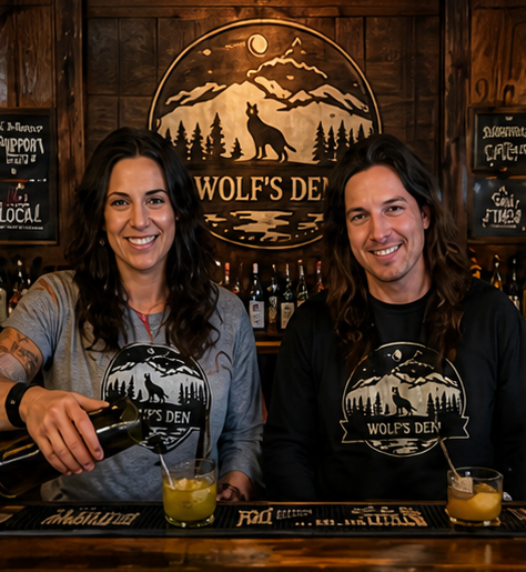 Two people behind a bar pour drinks in front of a Wolf’s Den sign