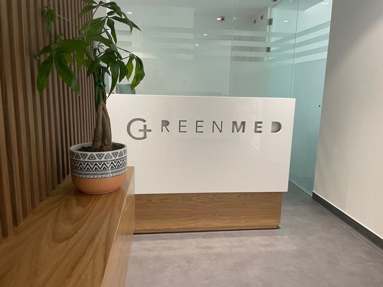 Receção da clínica Greenmed com balcão de atendimento e planta decorativa.