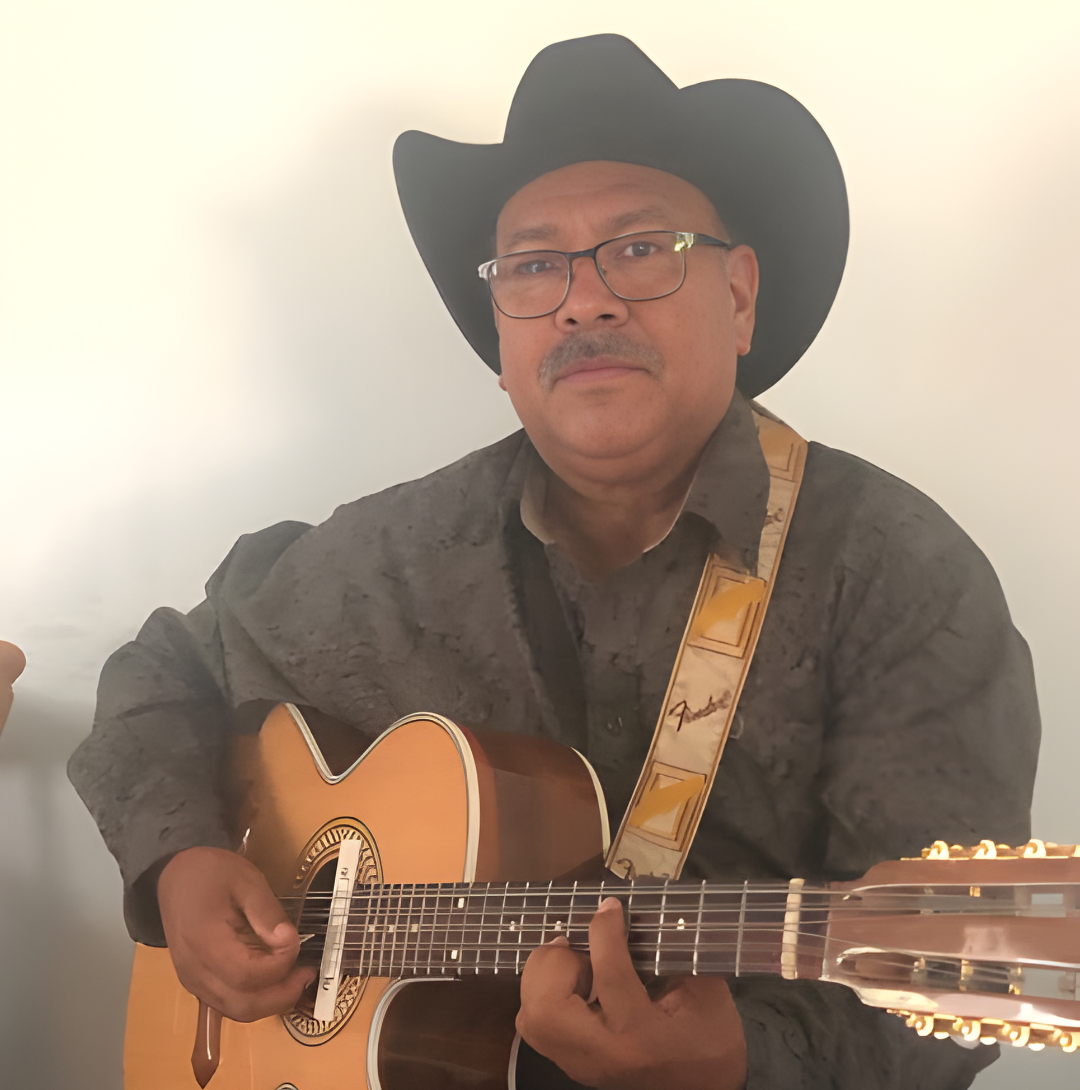 A person wearing a black cowboy hat and glasses plays an acoustic guitar against a plain white background.