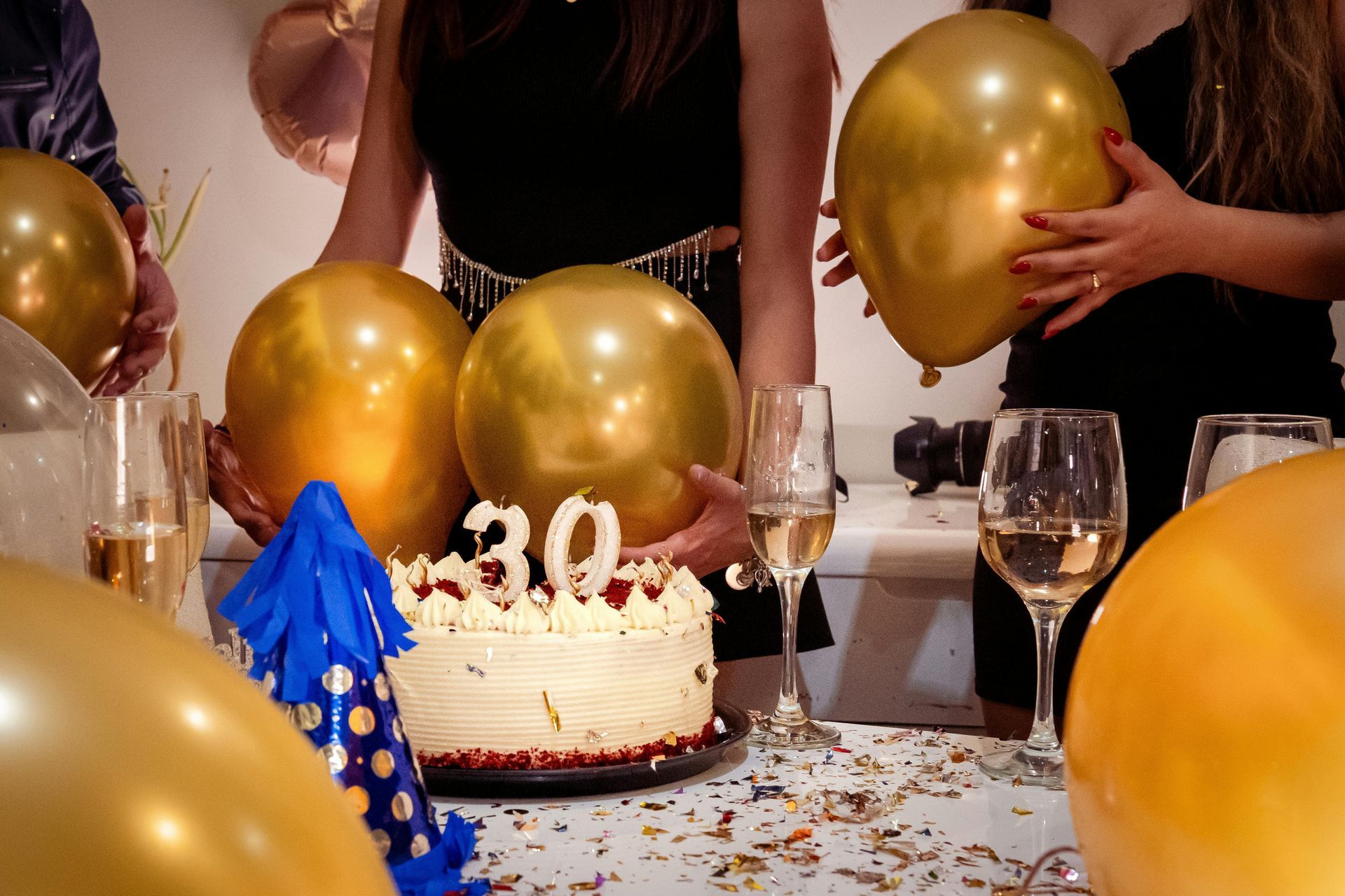 A birthday cake with a number 30 candle is surrounded by gold balloons, champagne glasses, and party decorations.