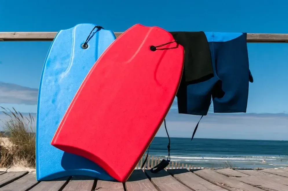 Three Boogie Boards Are Sitting on a Wooden Deck Near the Ocean — Hire All in Tugun, QLD