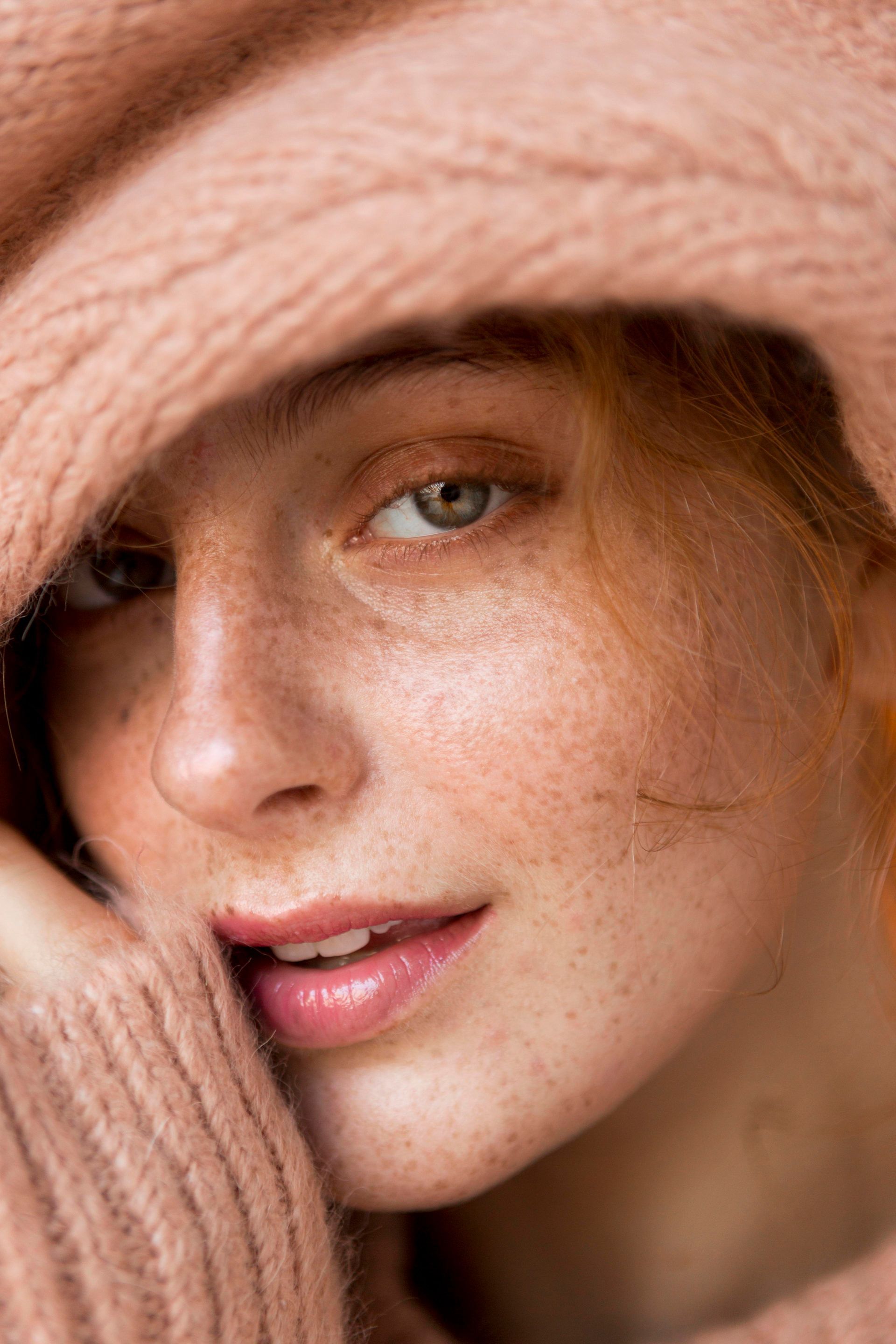 A close up of a woman 's face with freckles wearing a sweater and hat.