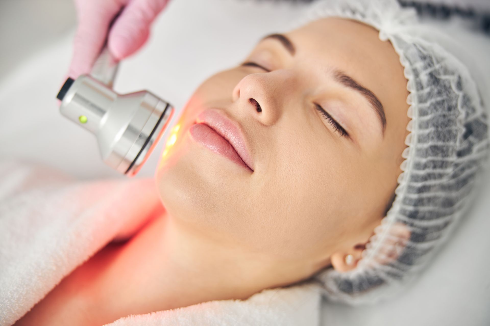 Close-up of a woman receiving LED light therapy on her face at a skincare clinic.