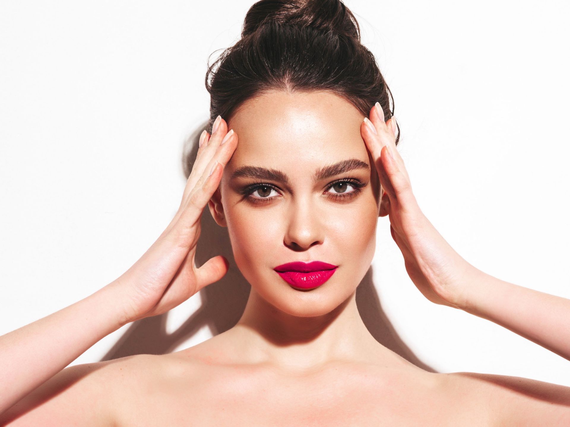 Close-up portrait of a woman with flawless skin, bold pink lips, and a stylish top bun.