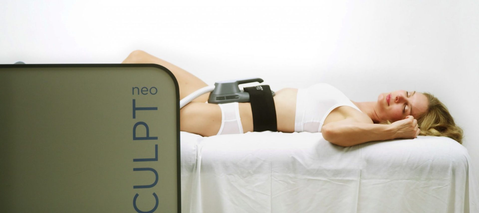 A woman is laying on a bed with a device that says sculpt on it