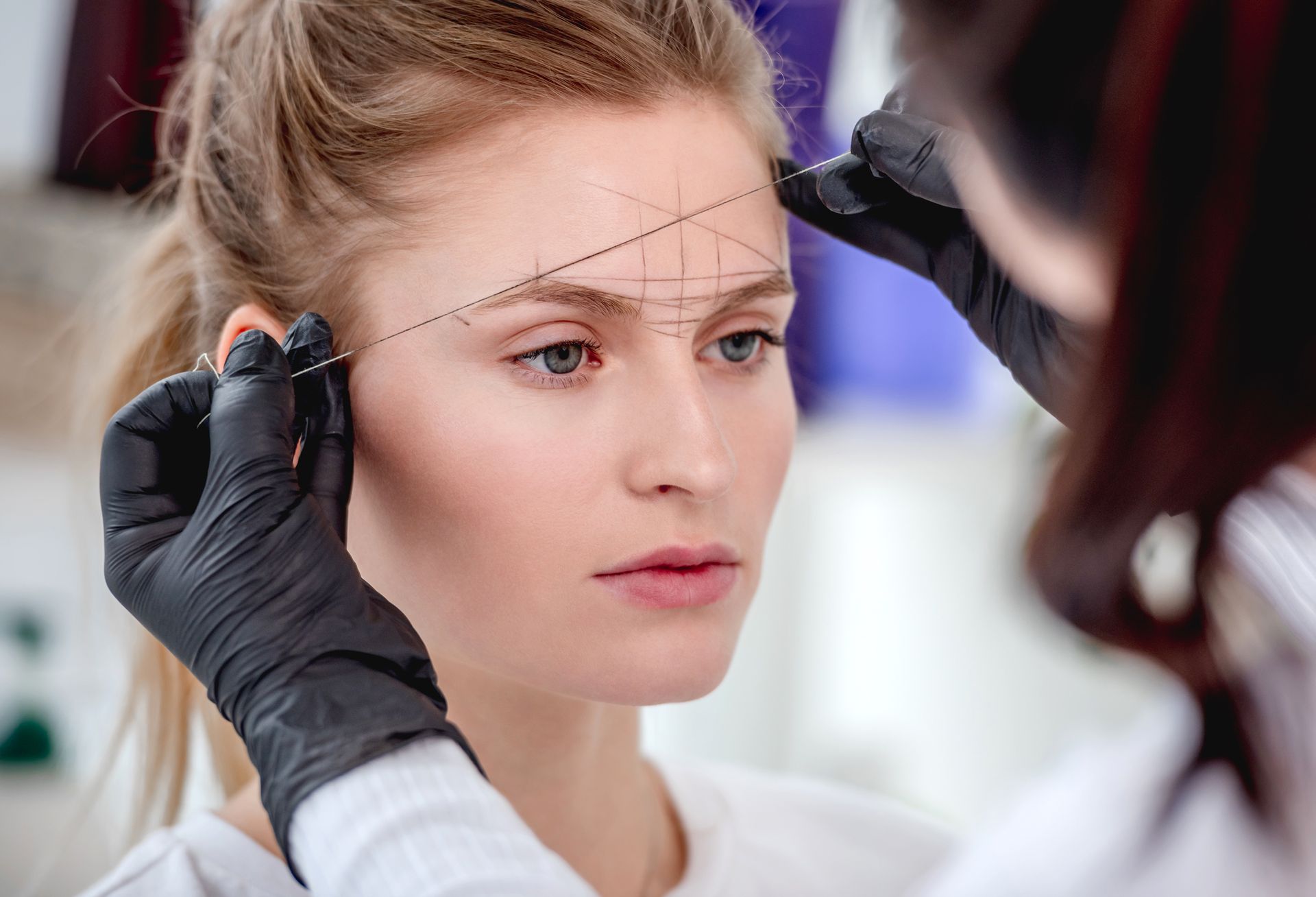 A woman is getting her eyebrows measured by a tattoo artist.