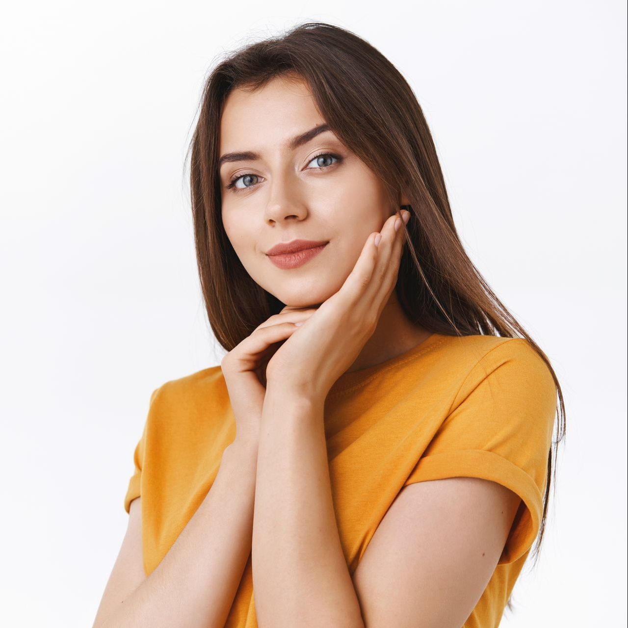 A woman in a yellow shirt is holding her face with her hands.