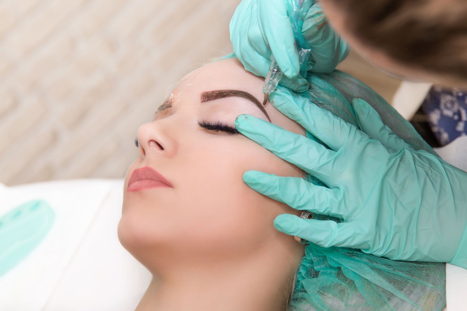 A woman is getting a semi - permanent makeup tattoo on her eyebrows.