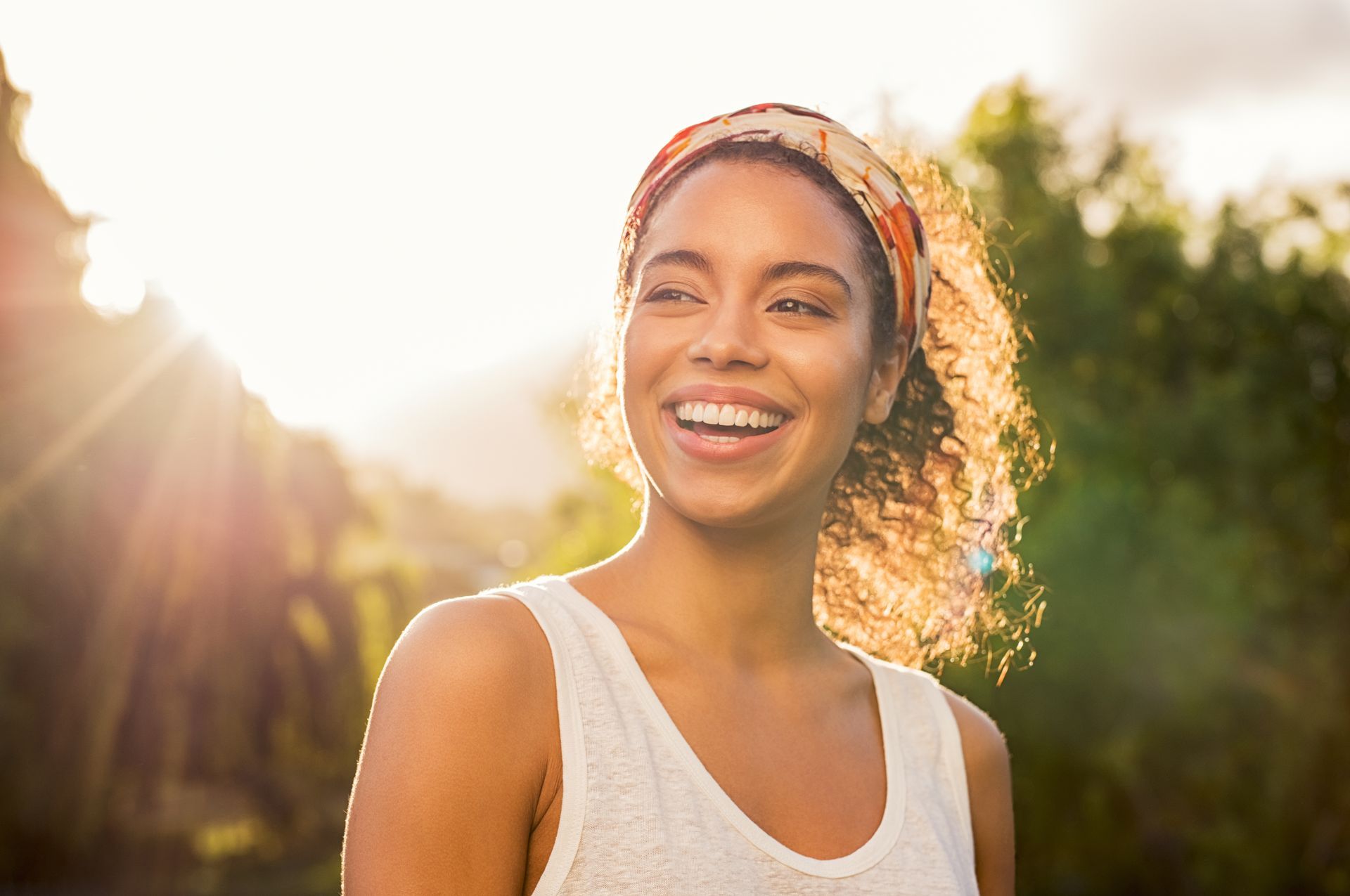 A woman wearing a headband is smiling in the sunlight.