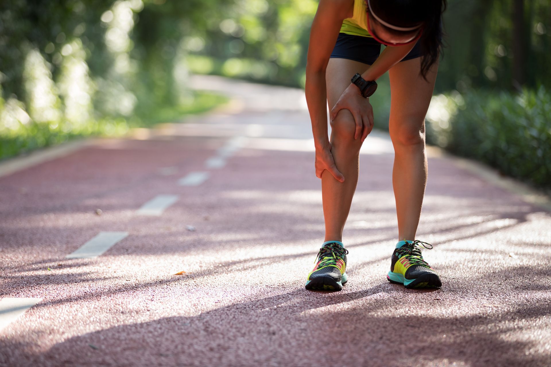 A woman is holding her knee while running on a track.