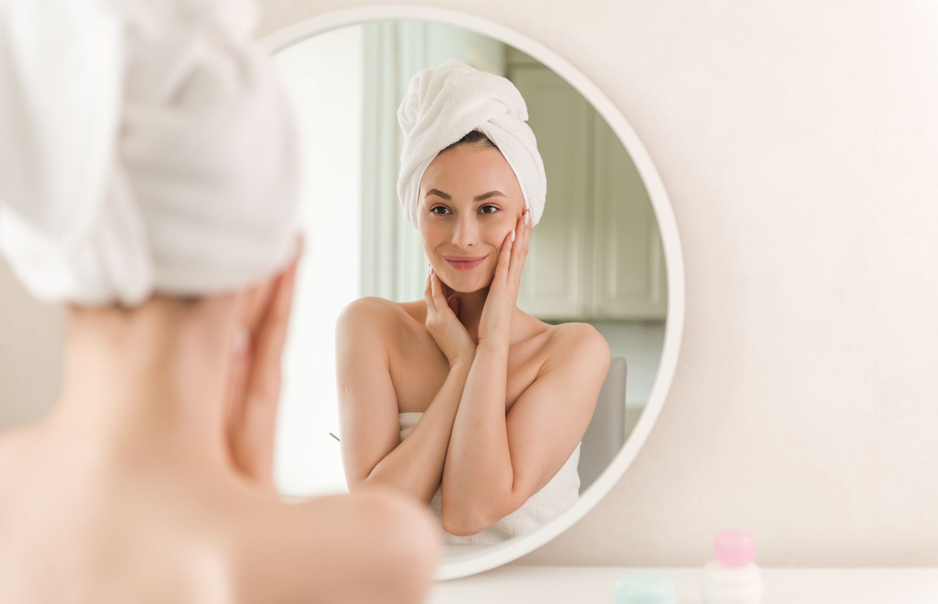 A woman with a towel wrapped around her head is looking at her reflection in a mirror.