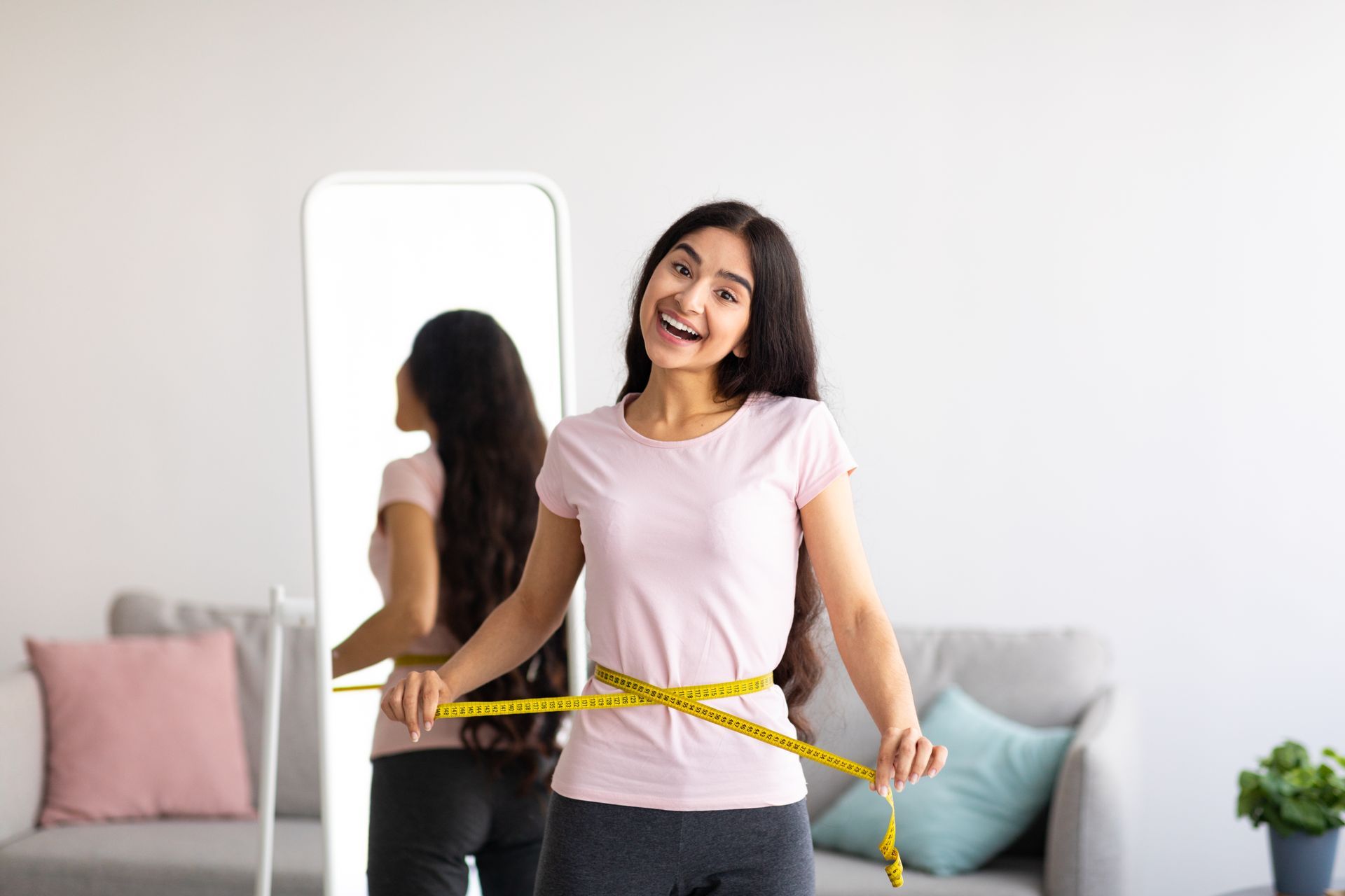 A woman is measuring her waist with a tape measure in front of a mirror.