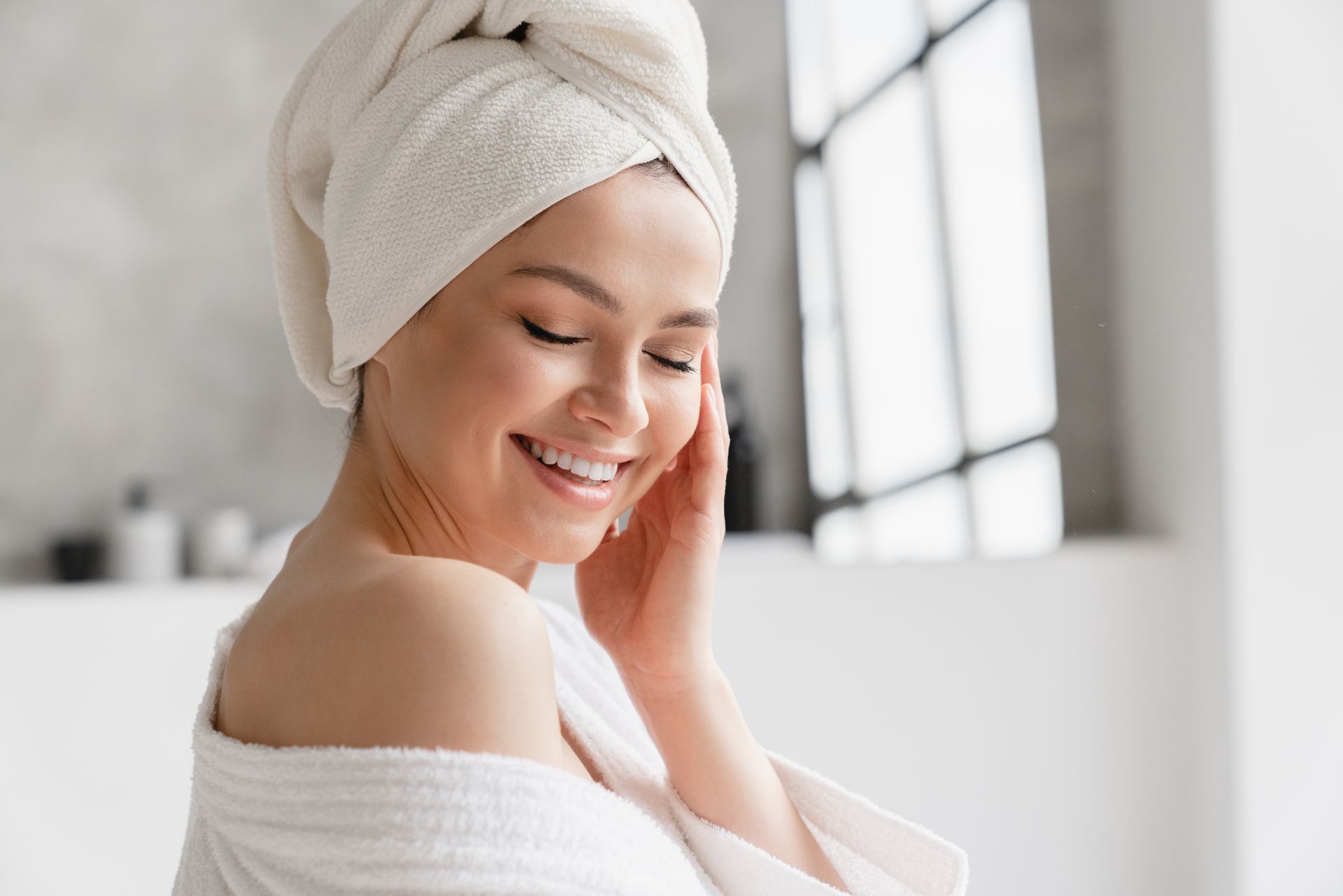 A woman with a towel wrapped around her head is smiling in a bathroom.
