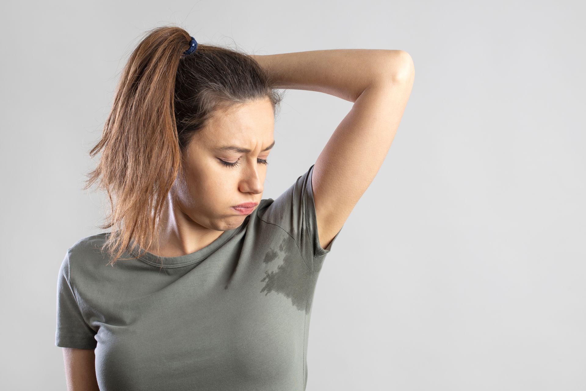 Woman with wet armpit stains, looking distressed, arm raised.